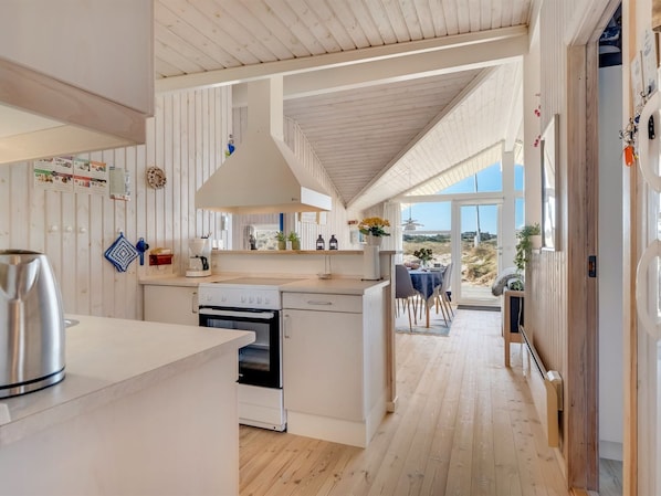 A modern kitchen with a central island, a dining area with a view, and a wooden ceiling.