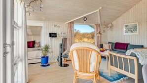 L’intérieur chaleureux d’un chalet avec un plafond en bois, un coin repas comprenant une table et des chaises, un canapé, un téléviseur et une grande fenêtre donnant sur le paysage extérieur.