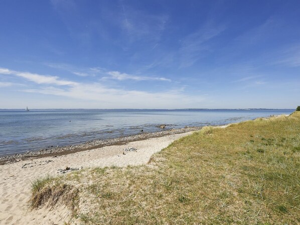 A beach with a clear sky, calm water, and a distant sailboat.