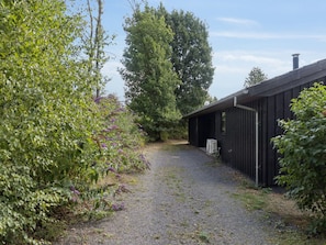 A gravel path leading to a black building with a chimney, surrounded by greenery and trees.