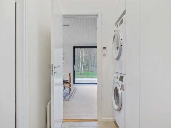 A laundry room with two washing machines and a door leading to a room with a view of trees.