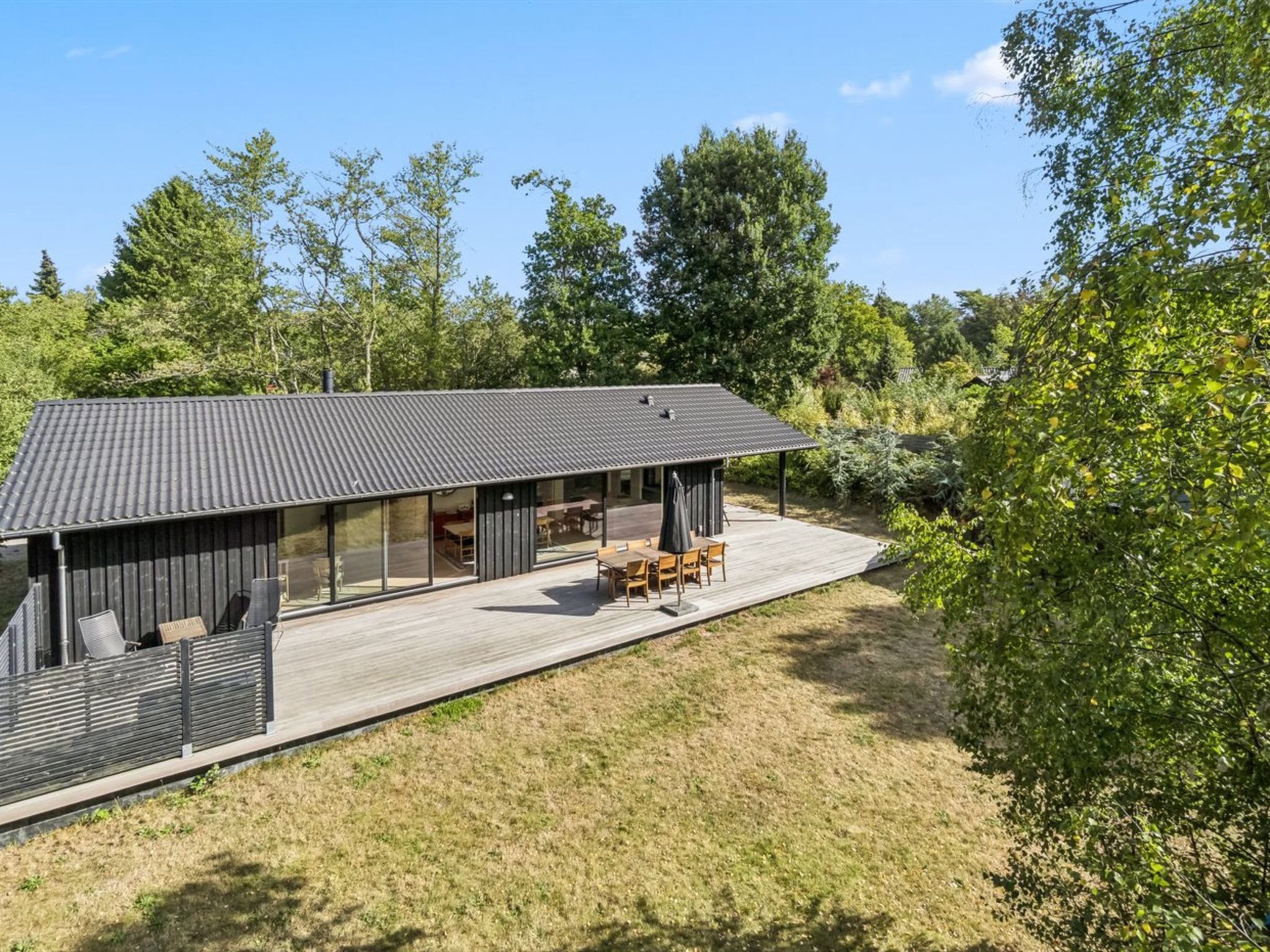 A modern house with a large deck, outdoor furniture, and a covered patio area.