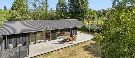 A modern house with a large deck, outdoor furniture, and a covered patio area.