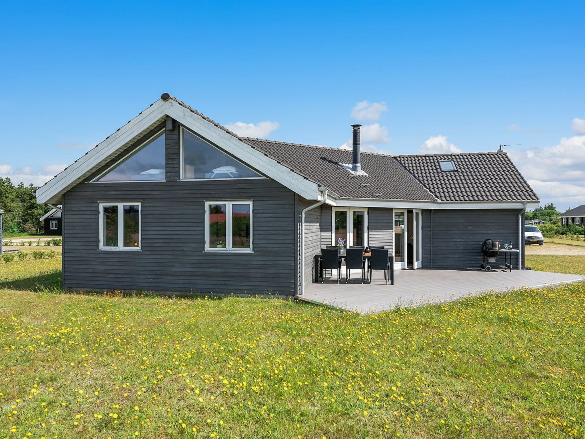 A modern house with a large glass window, a chimney, and a patio with outdoor furniture.