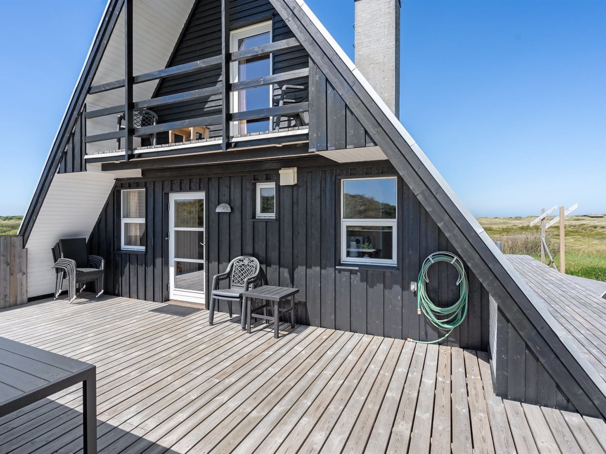 A two-story house with a wooden deck, a balcony, and a view of the beach.