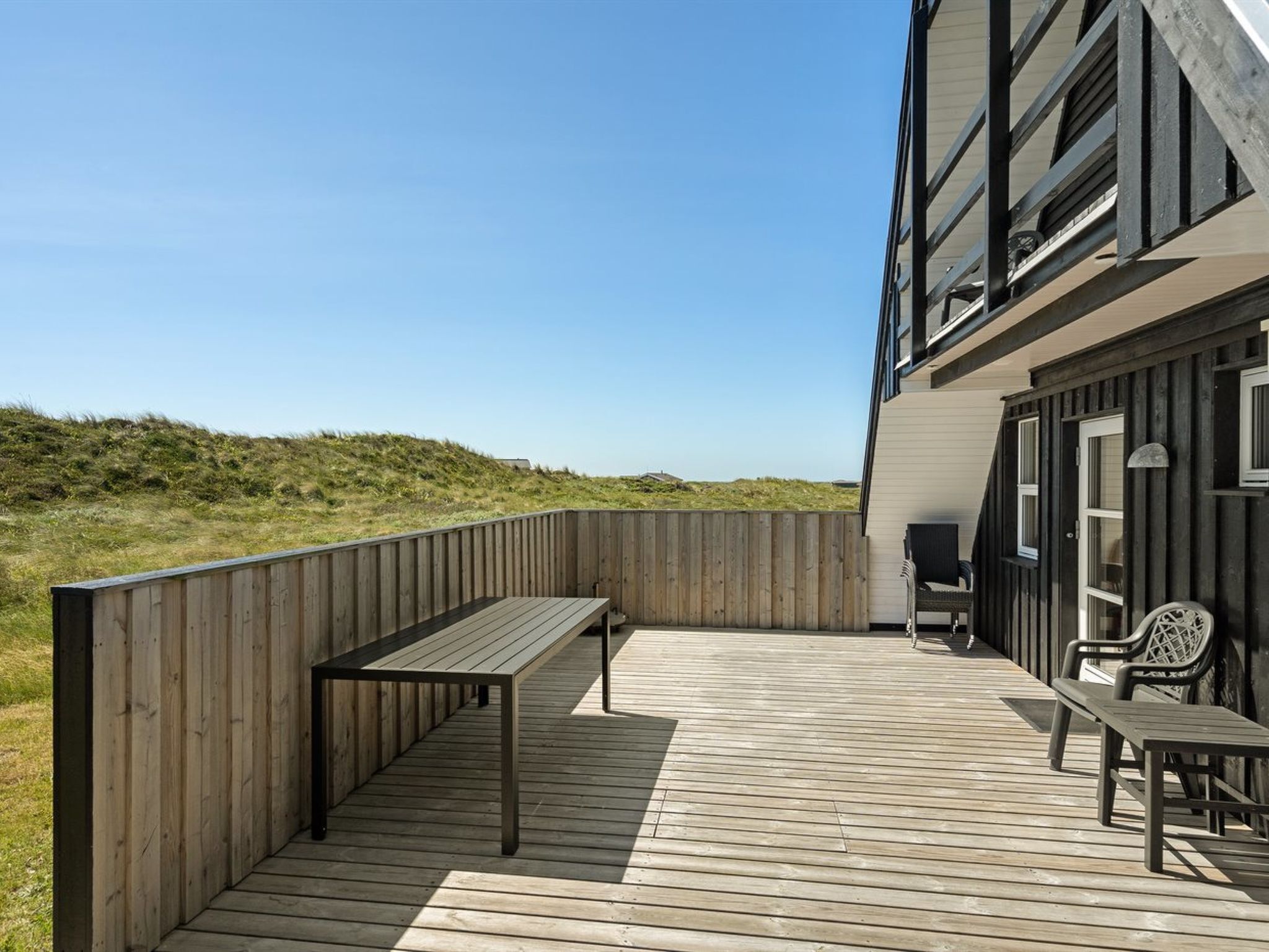 En træterrasse med bænk og bord, med udsigt over en græsplæne.
