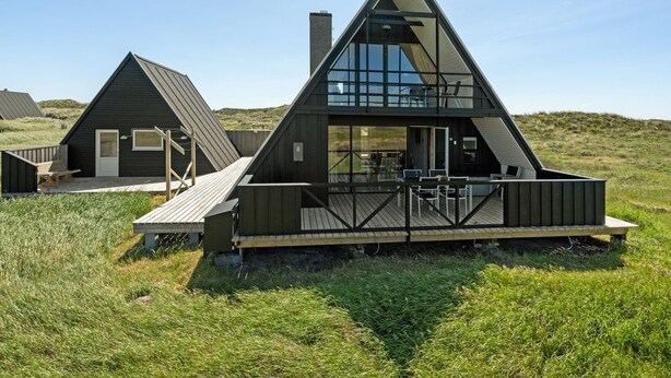 Een modern, driehoekig gebouw met een houten terras en glazen ramen, gelegen in een groene omgeving.