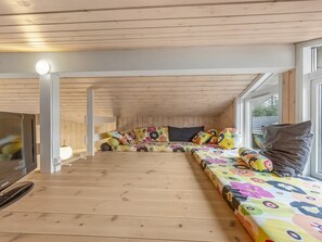 Ett mysigt rum med ett träpanelat tak, en soffa med färgglatt blommönstrat tyg och en tv på vänster sida.