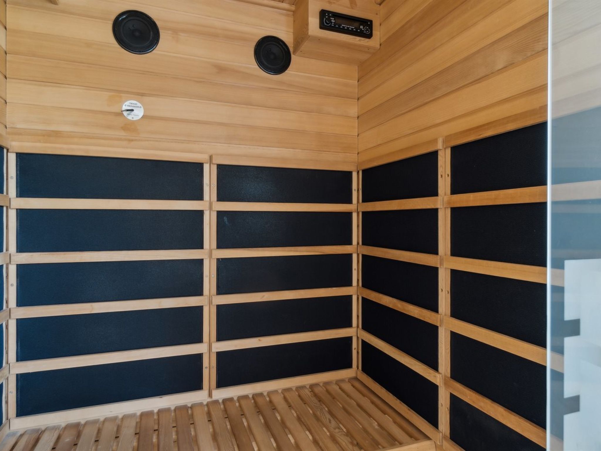 En sauna med trælameller og sorte paneler, et kontrolpanel og et ventilationssystem.