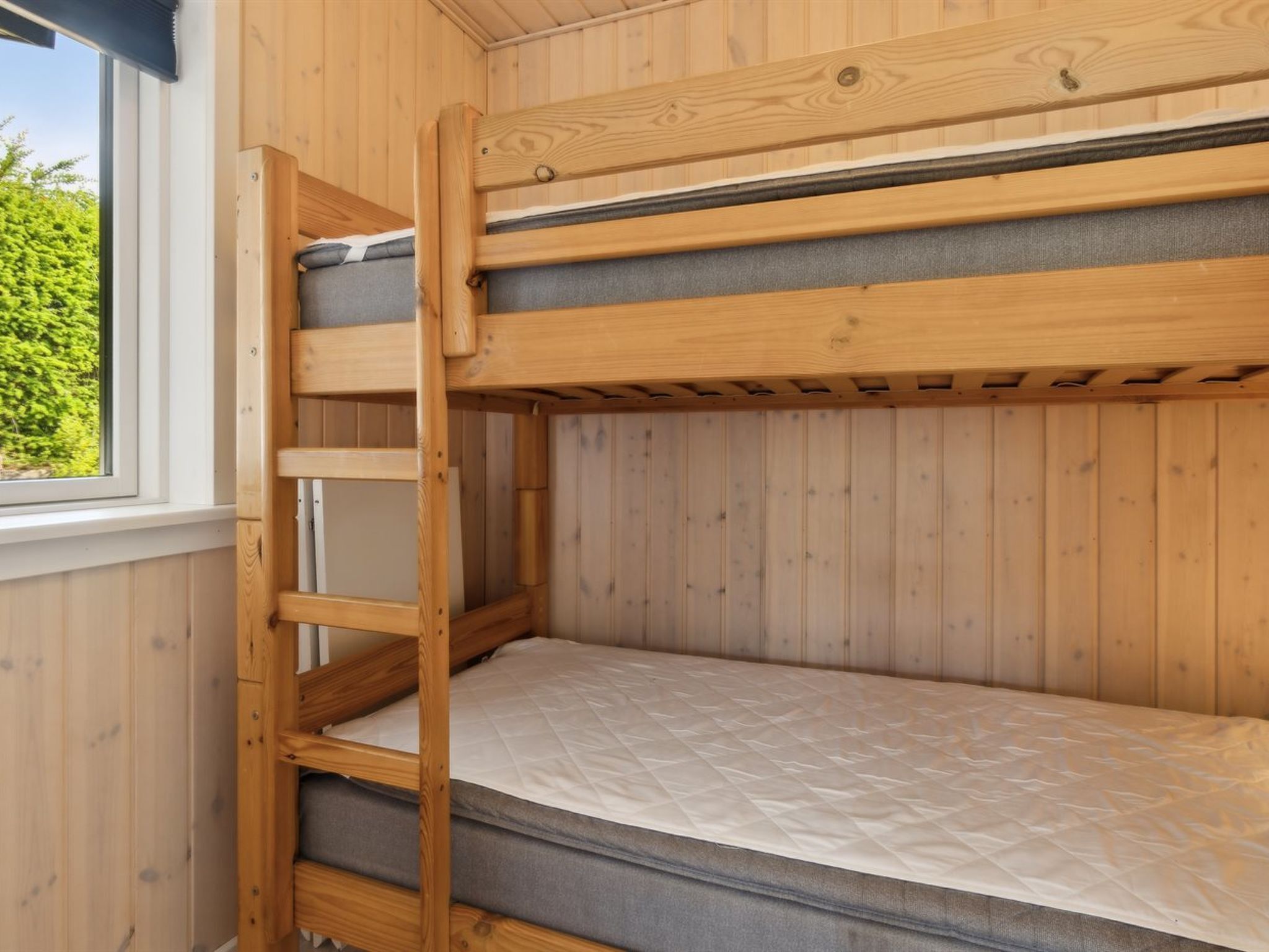 Uma cama beliche com escada, paredes de madeira e uma janela.