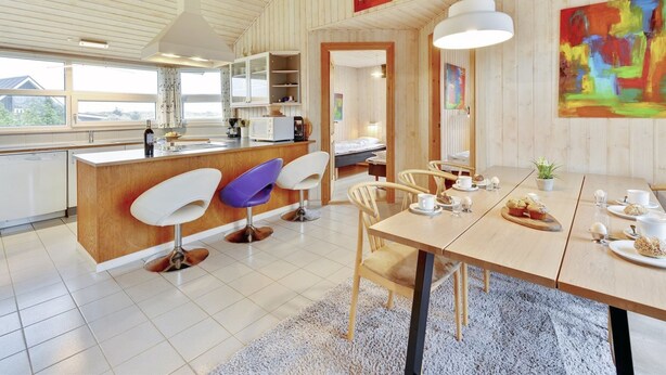 Cocina moderna con una isla central, asientos tipo bar y un comedor con una mesa preparada para dos.