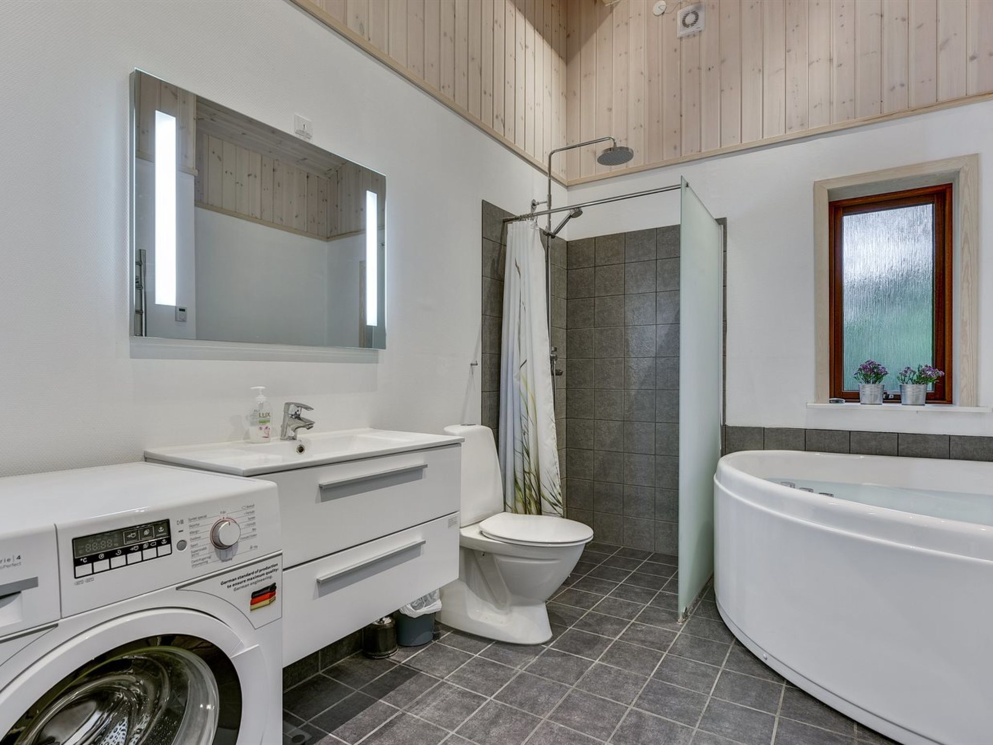 Et moderne badeværelse med vaskemaskine, toilet, bruser og badekar.