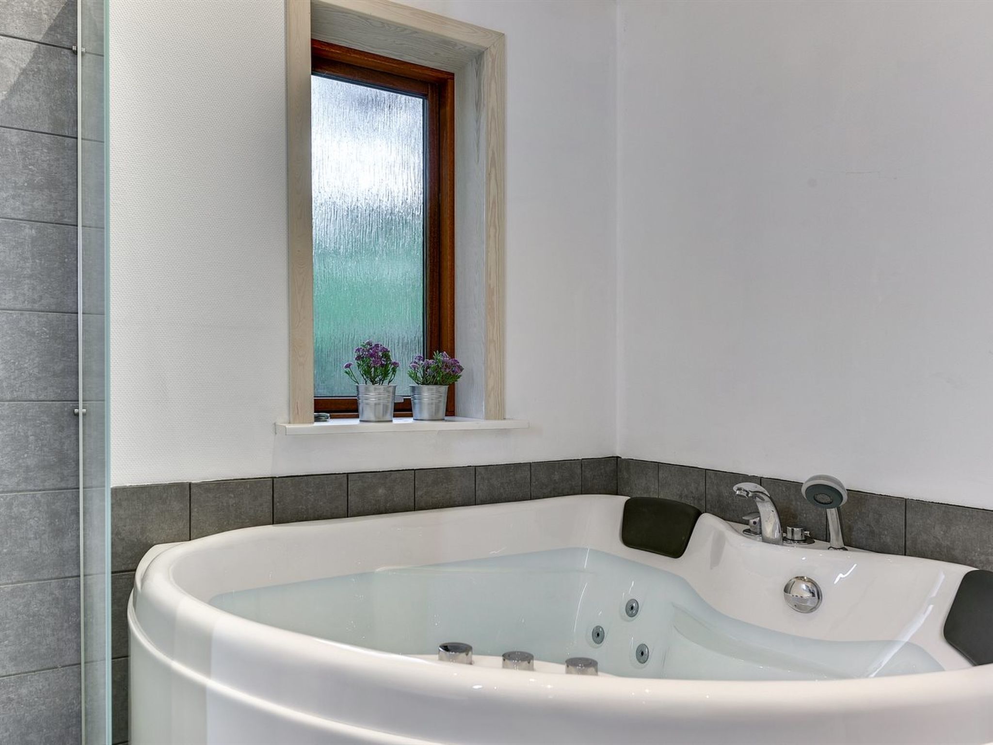 Une salle de bain moderne avec une baignoire sur pieds, une fenêtre à verre dépoli et une petite étagère ornée de plantes en pot.