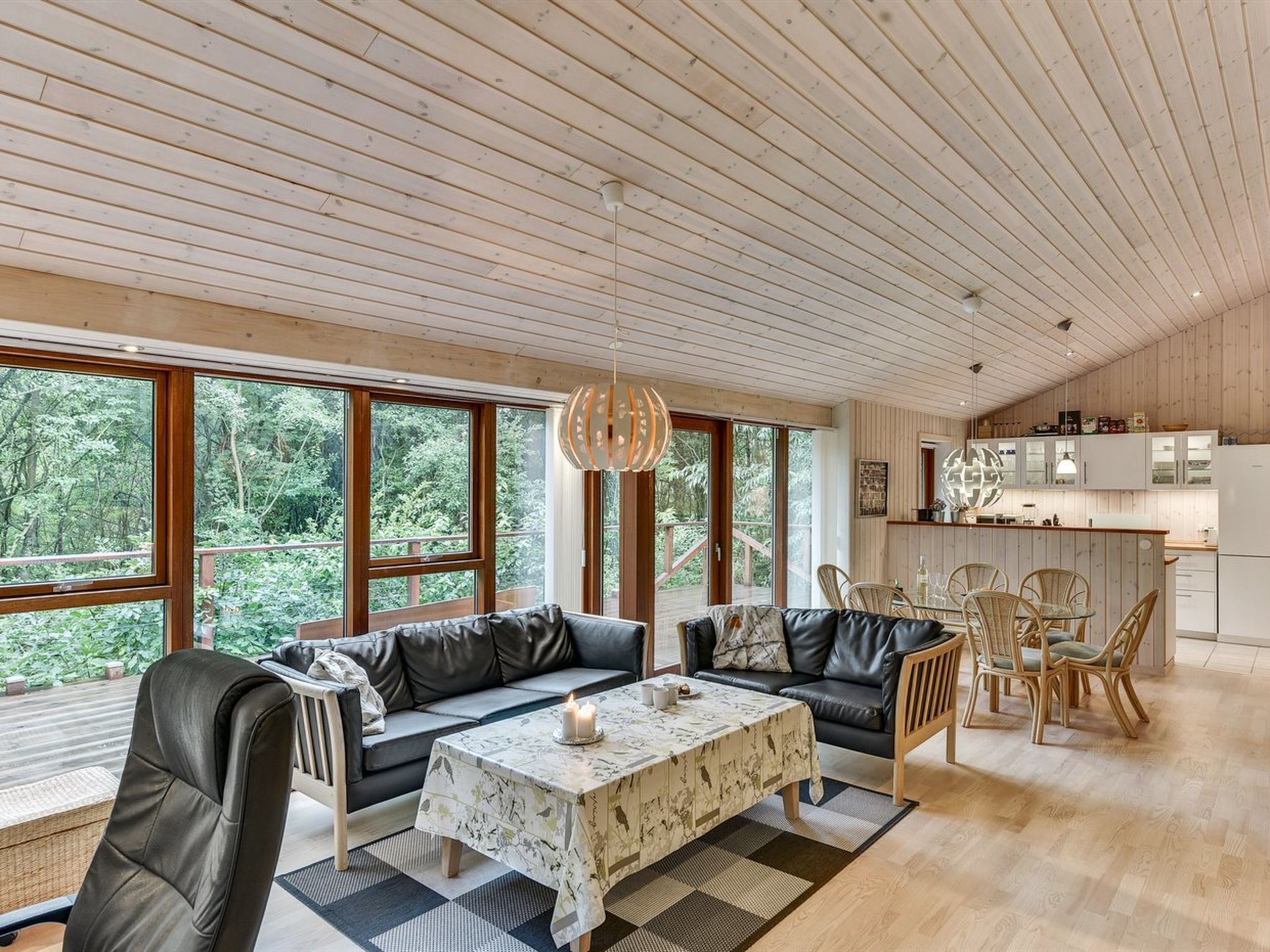 A spacious living area with a large window, a dining table, and a kitchen in the background.