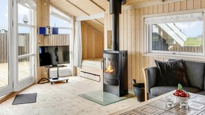 A cozy room with a wood-burning stove, a TV, a sofa, and a dining table with a bowl of fruit.