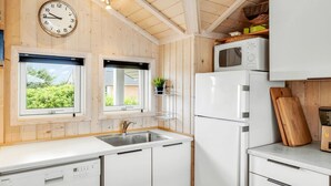 A kitchen with wooden walls, a clock, a sink, a dishwasher, a microwave, and a window with a view.