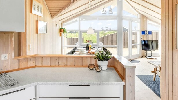 A modern kitchen with a large island, wooden paneling, and a view of the outdoors.