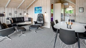 Een modern interieur met een houten plafond, een eethoek met een witte tafel en zwarte stoelen, een zwarte leren bank en een zwarte lederen fauteuil.