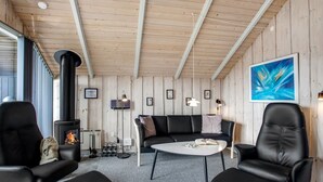 Een gezellige kamer met een zwarte leren bank, twee zwarte fauteuils, een kleine witte tafel en een houtkachel.