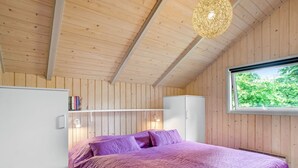 Een slaapkamer met een paars dekbed, witte kasten en een raam met uitzicht op groen.
