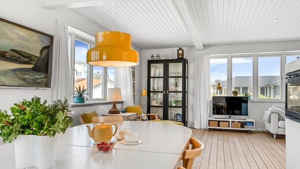 Uma sala de jantar moderna com uma mesa branca, luminária pendente amarela e vista da cidade através de grandes janelas.