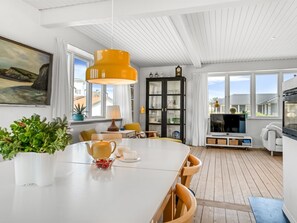 Un comedor moderno con una mesa blanca, una lámpara colgante amarilla y vistas a la ciudad a través de amplios ventanales.
