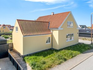 Une maison à deux étages, avec un toit recouvert de tuiles rouges, un petit porche à l’avant et une allée pavée.