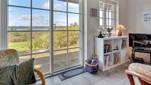 A room with large sliding glass doors, a white bookshelf, a television, and a piano. - "Tordis" - 250m to the fjord by Interhome (Roslev)