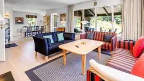 A spacious living room with a dark blue sofa, a striped sofa, and a wooden coffee table. There is a dining area with a table and chairs, and a kitchen area with a grill. - "Gullborg" - 800m from the sea by Interhome (Løkken)