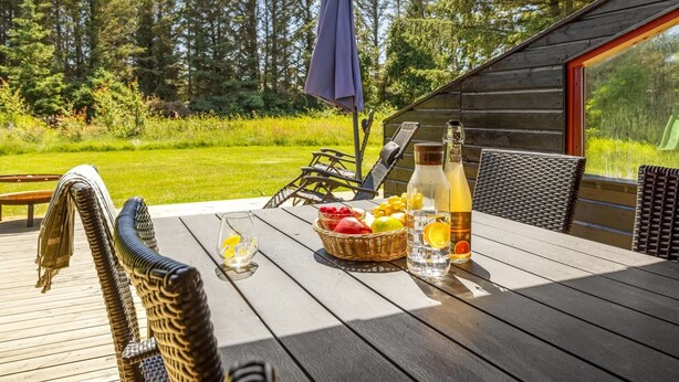 A wooden deck with wicker chairs, a table with fruits, a bottle, and a glass. - "Gullborg" - 800m from the sea by Interhome (Løkken)
