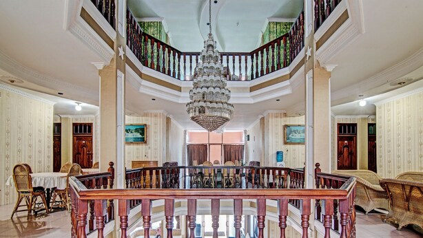 A grand interior with a central staircase, ornate chandelier, and classic furniture.
