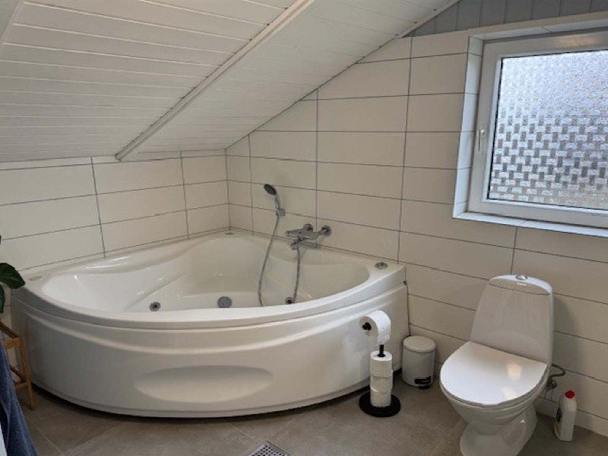 A modern bathroom with a large, curved bathtub, a toilet, and a window with a checkered pattern.