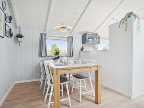 A dining area with a wooden table and white chairs, a hanging light fixture, and a window with curtains. - "Petrus" - 750m from the sea by Interhome (Hejls)