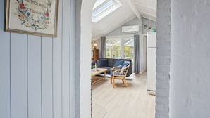 Un intérieur chaleureux avec un plancher en bois, un canapé et un fauteuil, dans une pièce dotée d’un plafond en pente et de lucarnes.
