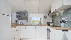 Une cuisine moderne avec des meubles blancs, un plan de travail en bois et une vue sur la verdure à l’extérieur.