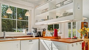 A modern kitchen with white cabinetry, a wooden countertop, and a built-in dishwasher. There are hanging lights, a window with a view of greenery, and a shelf with dishes and kitchenware. - "Eimi" - 1.5km from the sea by Interhome (Blokhus)