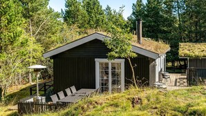 A small cabin with a sloped roof, a deck with outdoor seating, and a surrounding forest. - "Eimi" - 1.5km from the sea by Interhome (Blokhus)