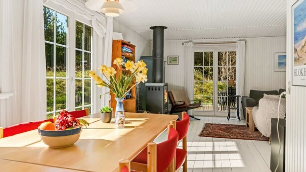 A spacious living room with a large wooden table, red chairs, a black stove, and a view of the outdoors through large windows. - "Eimi" - 1.5km from the sea by Interhome (Blokhus)