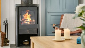 A cozy room with a wood-burning stove, a door, a table with candles, and a wicker basket. - "Eimi" - 1.5km from the sea by Interhome (Blokhus)