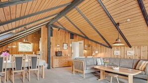 Un loft espacioso con techo alto, paredes de madera, zona de comedor con sillas y mesa, sofá y área de cocina con armarios y encimera.