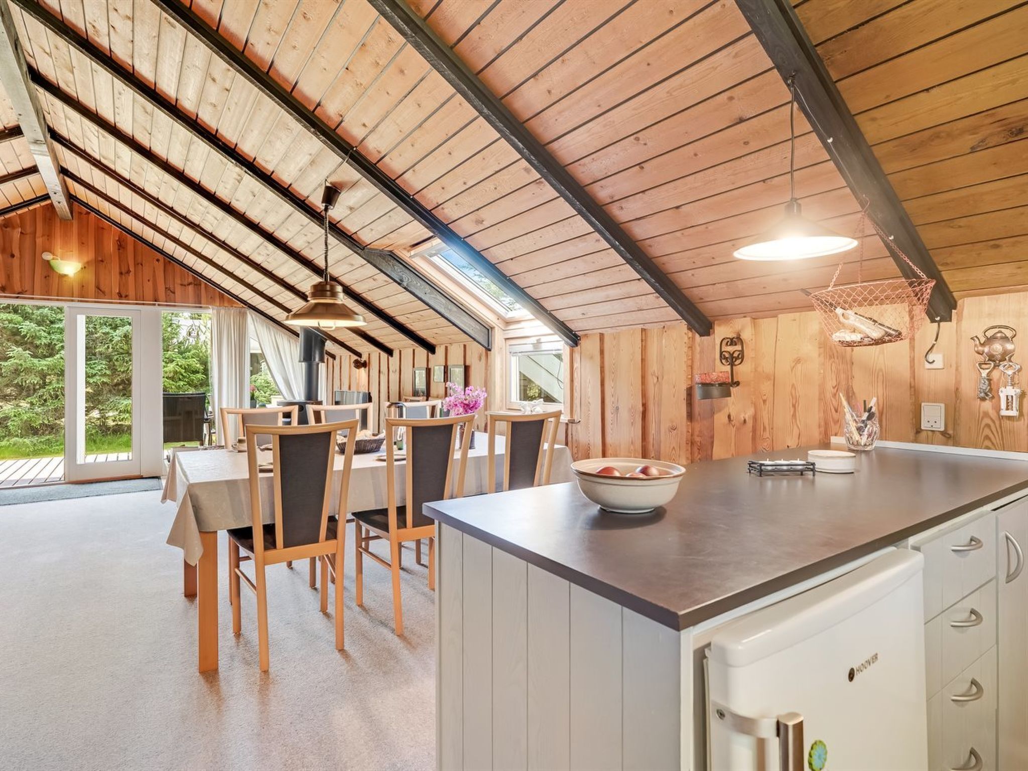 A modern kitchen with a central island, wooden dining area, and a view of the outdoors.