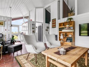 Ein modernes Wohnzimmer mit einem Holztisch, zwei karierten Stühlen, einem schwarzen Ledersofa und einem Bücherregal.