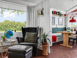 Ein modernes Wohnzimmer mit einem schwarzen Ledersessel, einem runden Tisch mit Globus, einem Holztisch und Blick auf Grünflächen außerhalb.