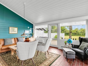 A room with a teal wall, a wooden ceiling, a large window, a sofa, two chairs, a coffee table, and a rug.