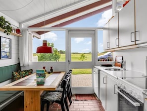 Eine Küche mit Blick ins Freie, ein Essbereich mit Tisch und Stühlen sowie eine rote Pendelleuchte.