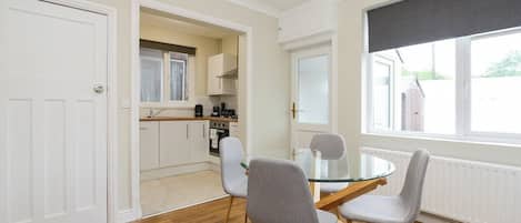 A modern kitchen with white cabinets, a dining table with four chairs, and a large window with a view of the outside.