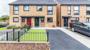 A two-story residential building with a brick facade, a red door, and a car parked in the driveway. - A Stylish, essential 3bed Home with Secure Parking (Nottingham)
