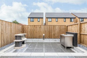 A backyard with a barbecue area, a stone bench, and a stainless steel sink.