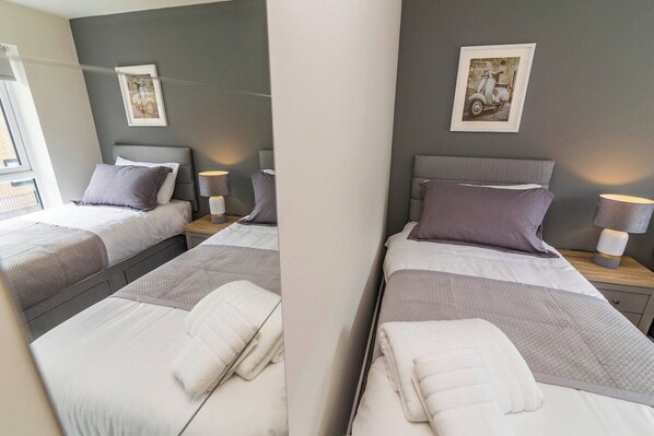 A hotel room with two beds, each with a pillow and a bedside table with a lamp.