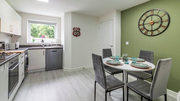 A modern kitchen with a dining area, a clock on the wall, and a window with a view. - A Stylish, essential 3bed Home with Secure Parking (Nottingham)